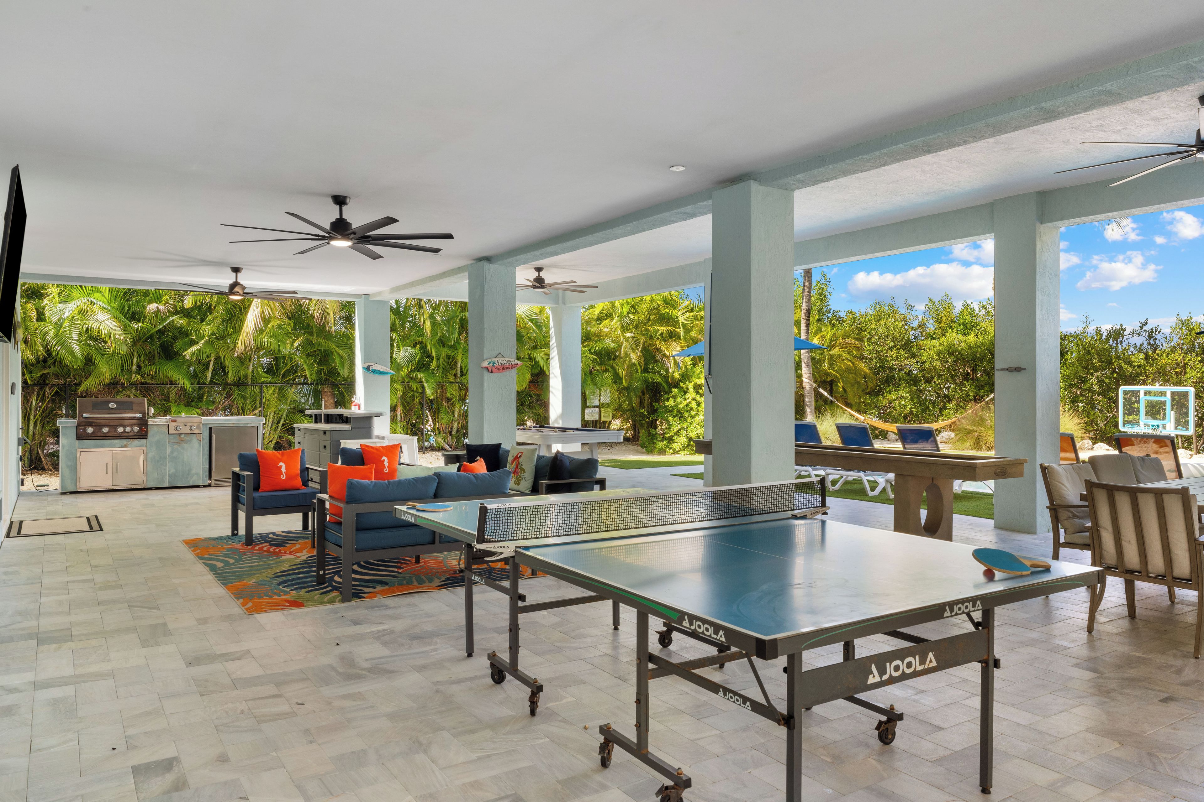 An outdoor patio with a ping pong table, seating area, and a barbecue grill.