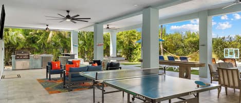 An outdoor patio with a ping pong table, seating area, and a barbecue grill.