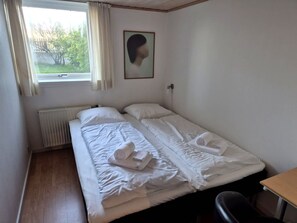 Ein Einzelzimmer mit Fenster, Heizkörper, Schreibtisch und Stuhl.