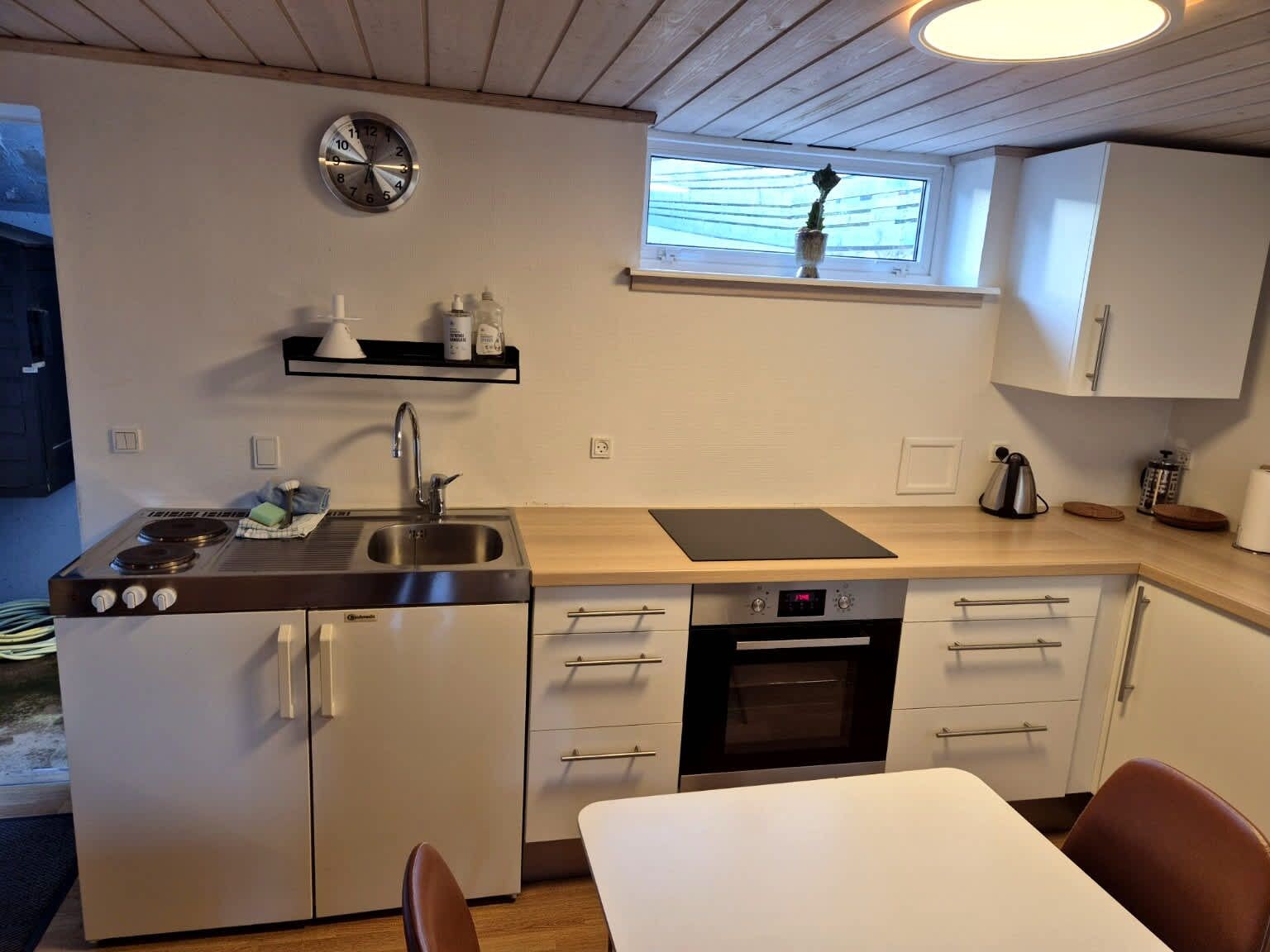 A compact kitchen with a stove, sink, oven, and a clock on the wall.