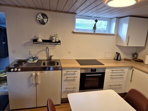 Eine kleine Küche mit Herd, Spüle, Backofen und einer Uhr an der Wand.