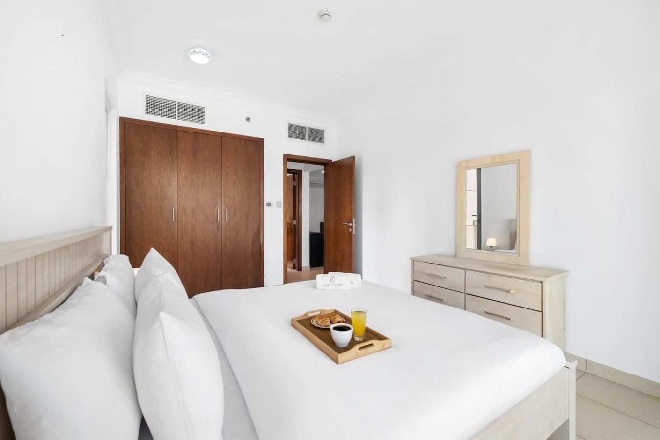 A hotel room with a bed, wooden wardrobe, a dresser, and a tray with breakfast items.