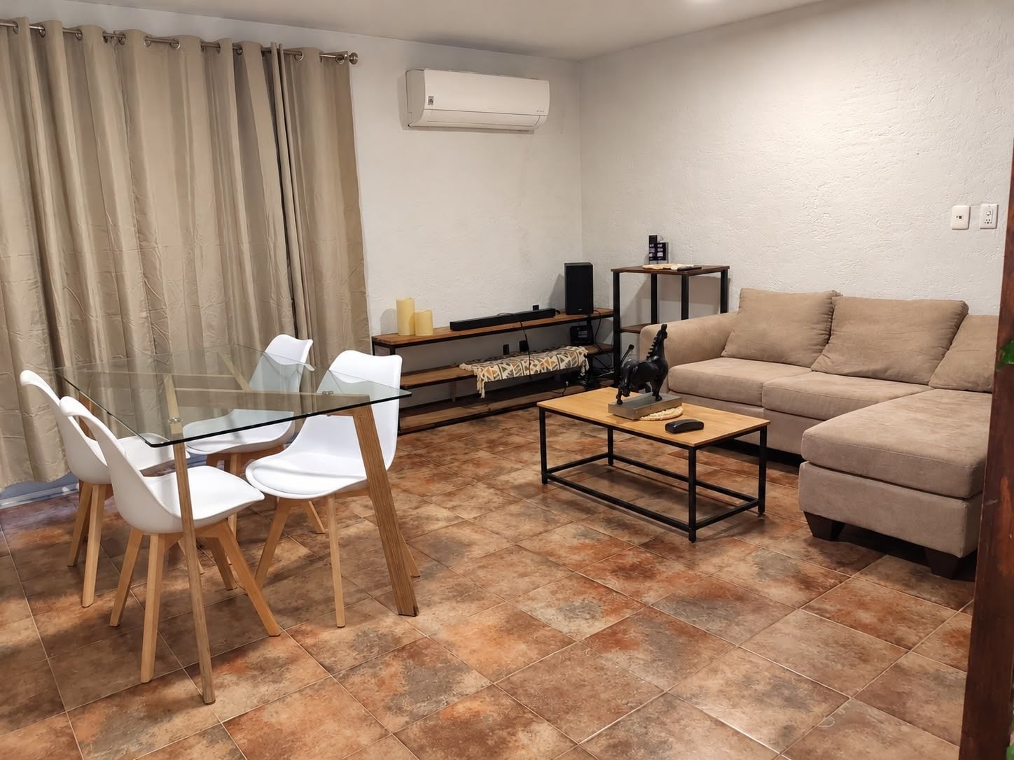 Un salon avec une table en verre, des chaises blanches, un canapé beige et une table basse.