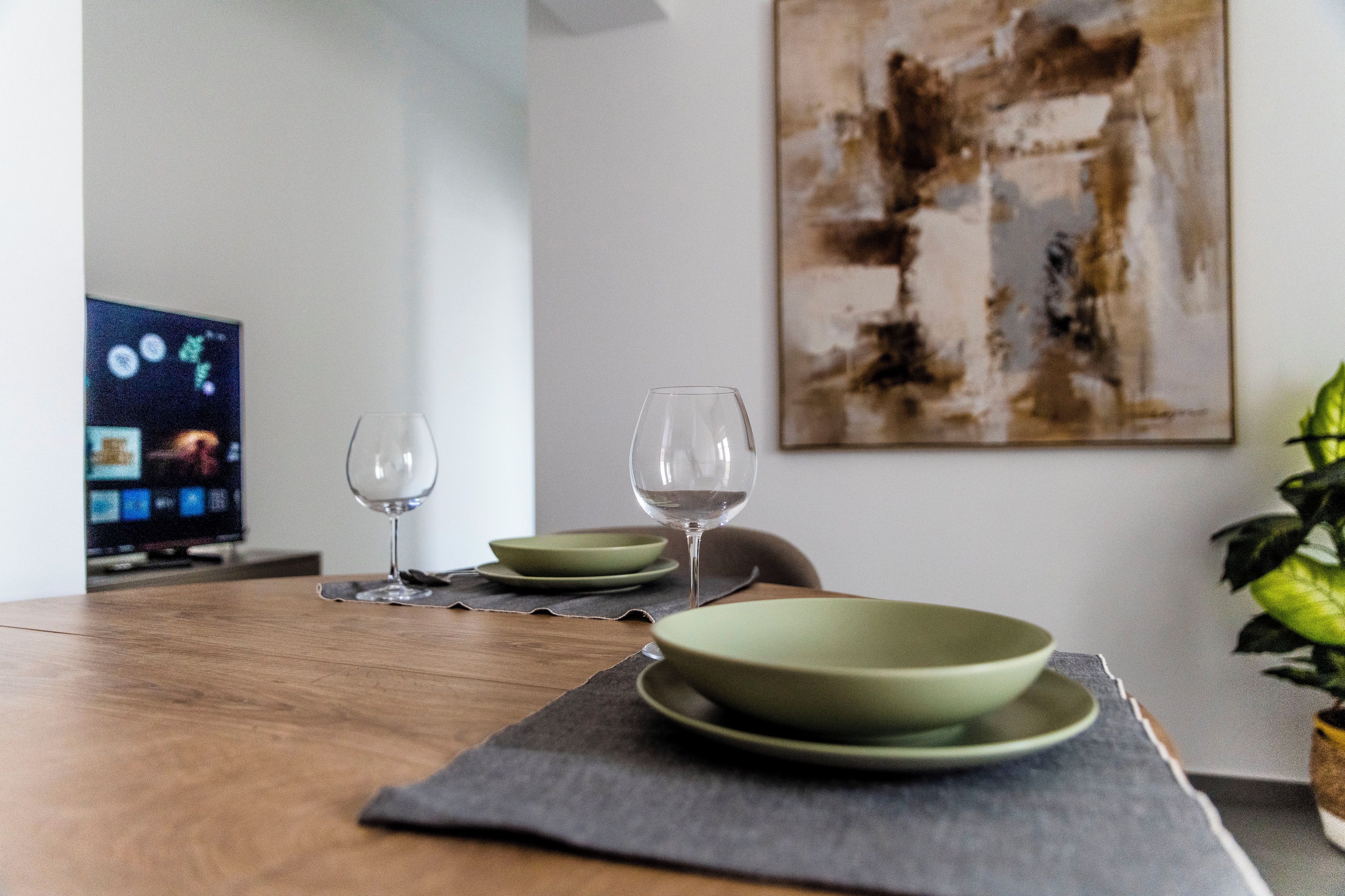 A dining table with a placemat, two wine glasses, and a green bowl set.
