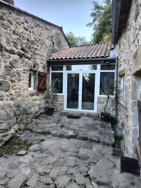 A stone building with a tiled roof, a glass door entrance, and a potted plant.