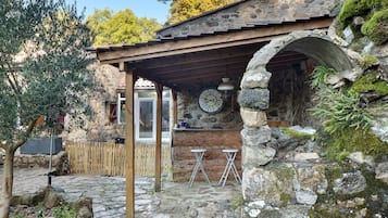 Un edificio rústico de piedra con una pérgola de madera, paredes de piedra y un reloj de piedra.