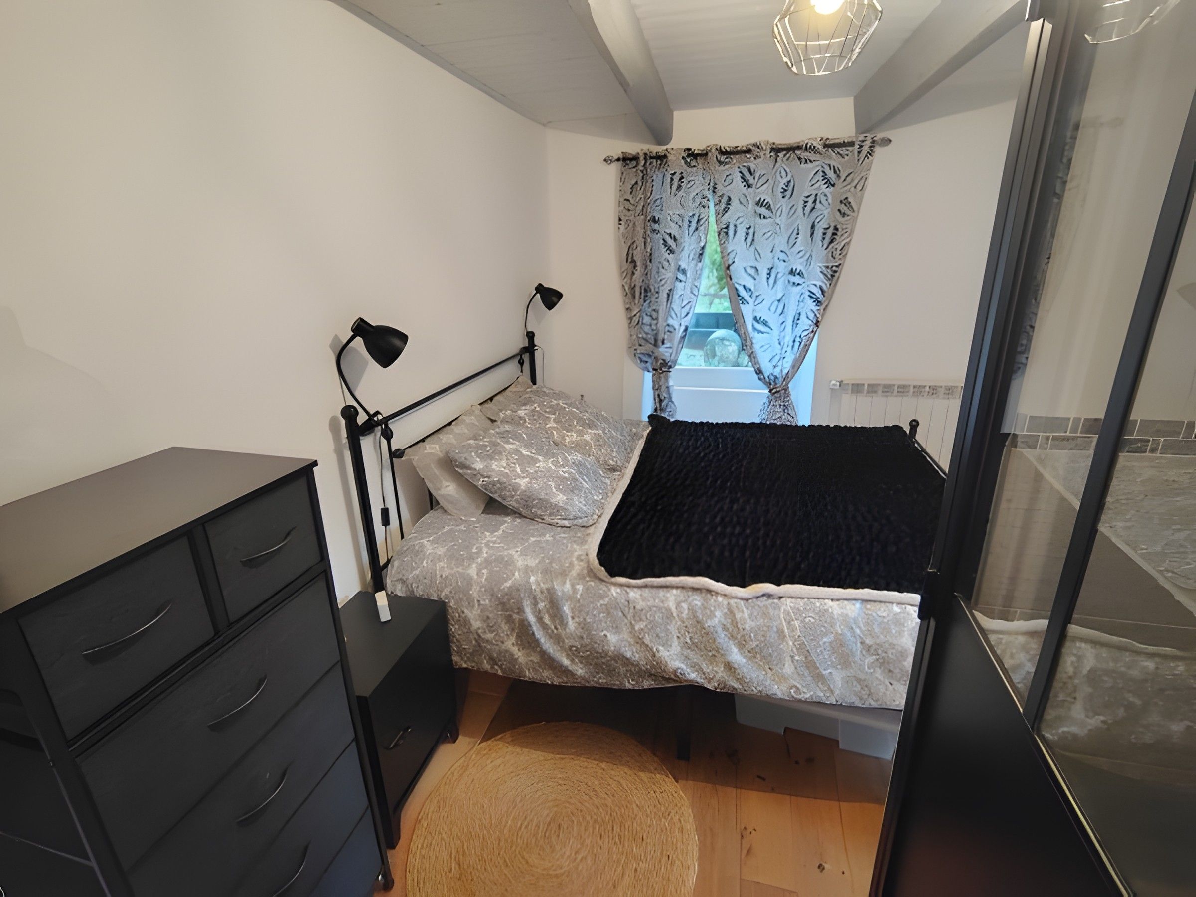 Un dormitorio con cama, mesita de noche, lámpara, cómoda y ventana con cortinas.