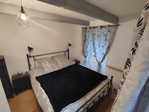 A bedroom with a bed, a bedside lamp, a window with curtains, and a hanging light fixture.
