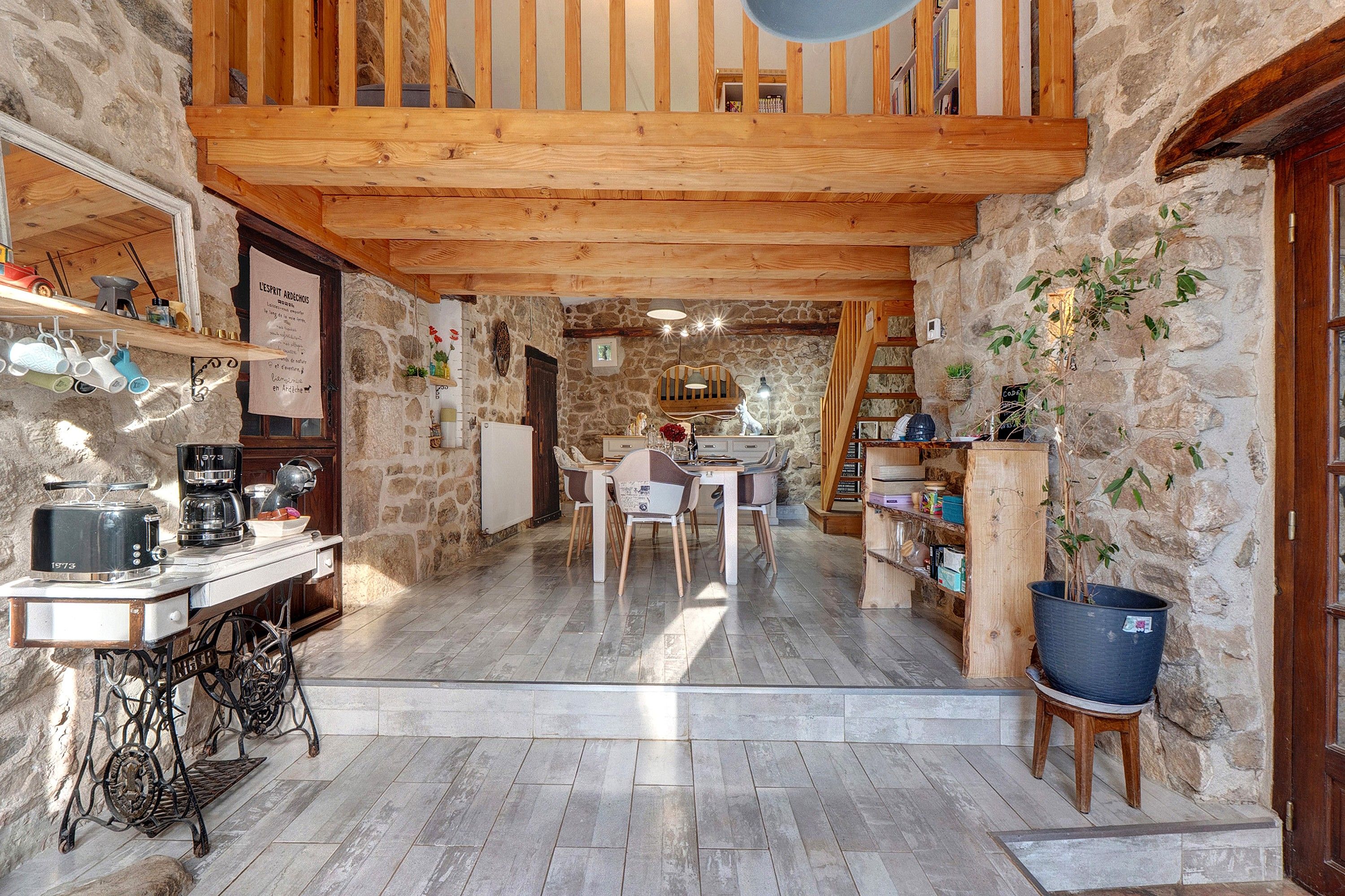 Une cuisine rustique aux murs de pierre, avec des poutres en bois et un coin repas comprenant une table et des chaises.