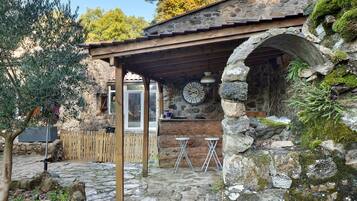 Un edificio rústico de piedra con una pérgola de madera, paredes de piedra y un reloj de piedra.