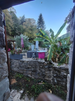 A stone wall with a garden area, including a seating area with a table and chairs, a pink barrel, and a statue. - Bed and Breakfast 'Evasion' at the La Vie est Belle Breeding Farm (Boucieu-le-Roi)