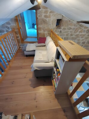 An attic room with a wooden floor, a white sofa, a bookshelf, and a stone wall. - Bed and Breakfast 'Evasion' at the La Vie est Belle Breeding Farm (Boucieu-le-Roi)
