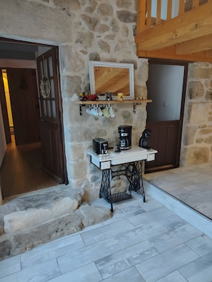 A stone-walled room with a vintage sewing machine table, a coffee station, and a shelf with mugs and a toy car. - Bed and Breakfast 'Evasion' at the La Vie est Belle Breeding Farm (Boucieu-le-Roi)