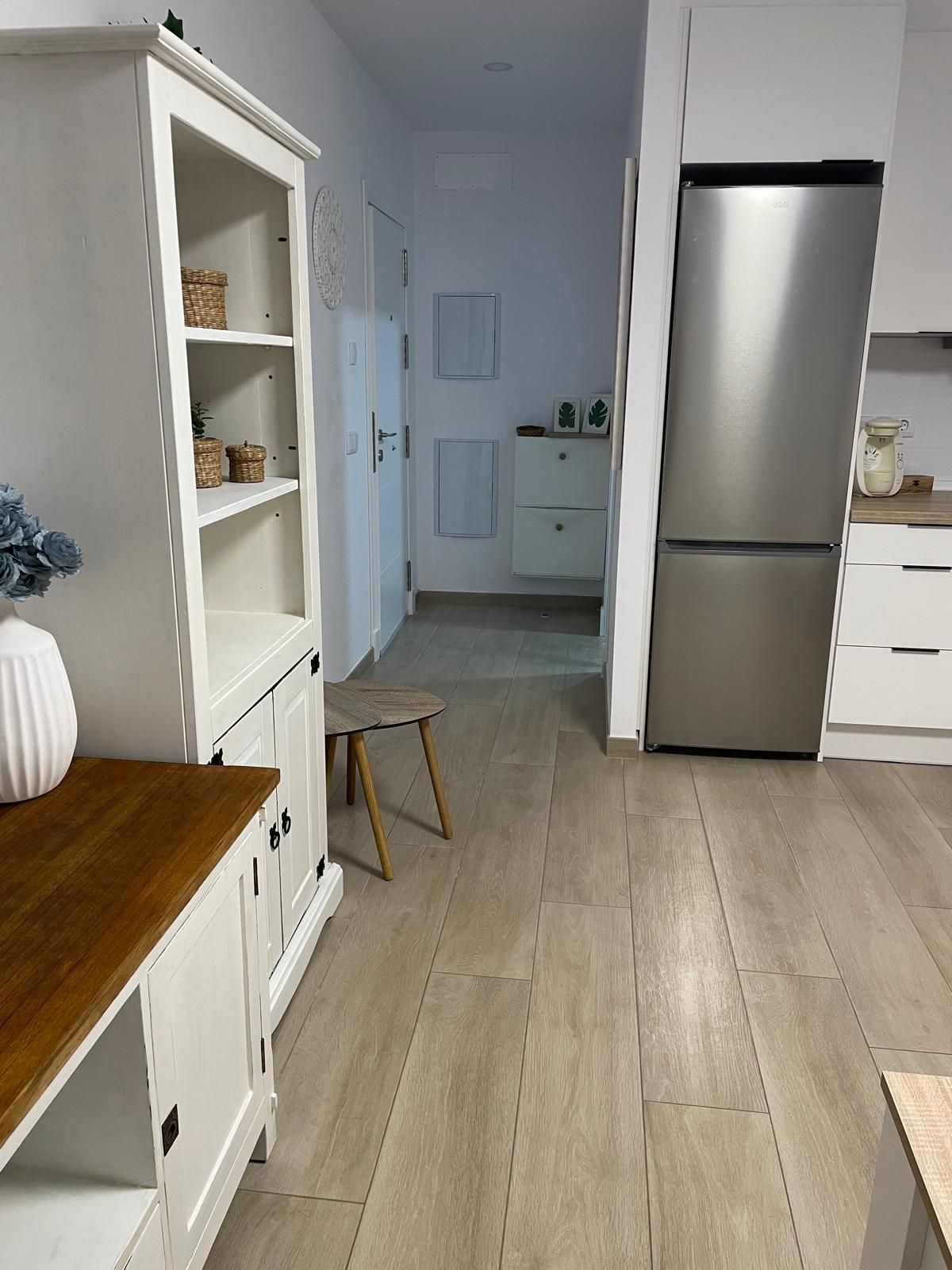 A modern kitchen with white cabinetry, a stainless steel refrigerator, and a wooden dining table.