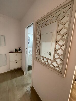 Un passadís amb una porta blanca, un moble petit amb calaixos i un panell decoratiu amb un dibuix geomètric.