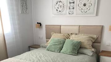 Una cama bien hecha con cubrecolcha acolchado, una mesita de noche con lámpara y cuadros en la pared sobre la cama.