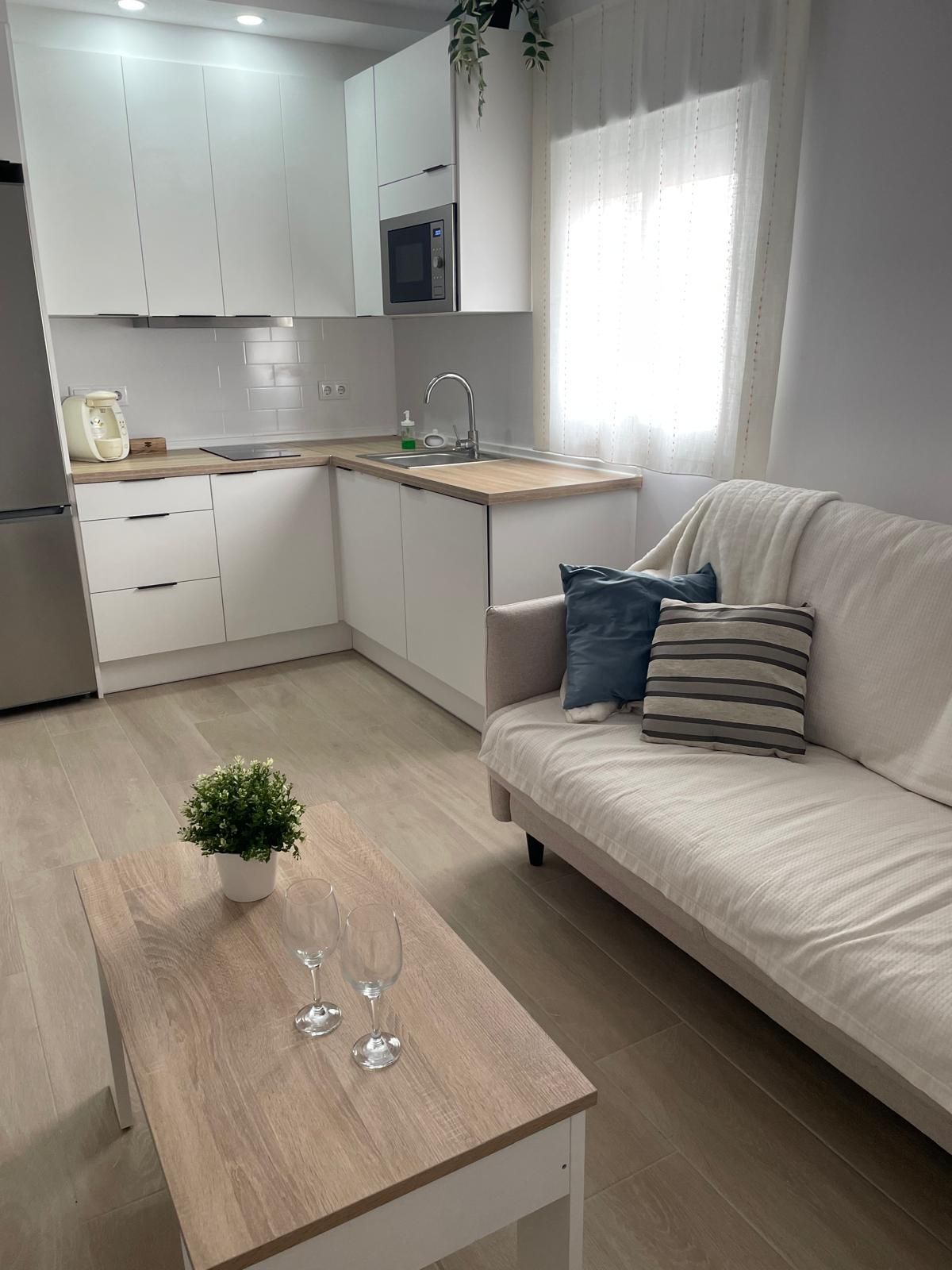 Una cocina moderna con armarios blancos, microondas integrado y encimera de madera.