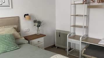 A bedroom with a bed, bedside table, lamp, radiator, and a wardrobe with hangers.