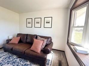 A brown leather sofa with two cushions, a patterned rug, and three framed pictures on the wall. - Country getaway + private pond (Creal Springs)