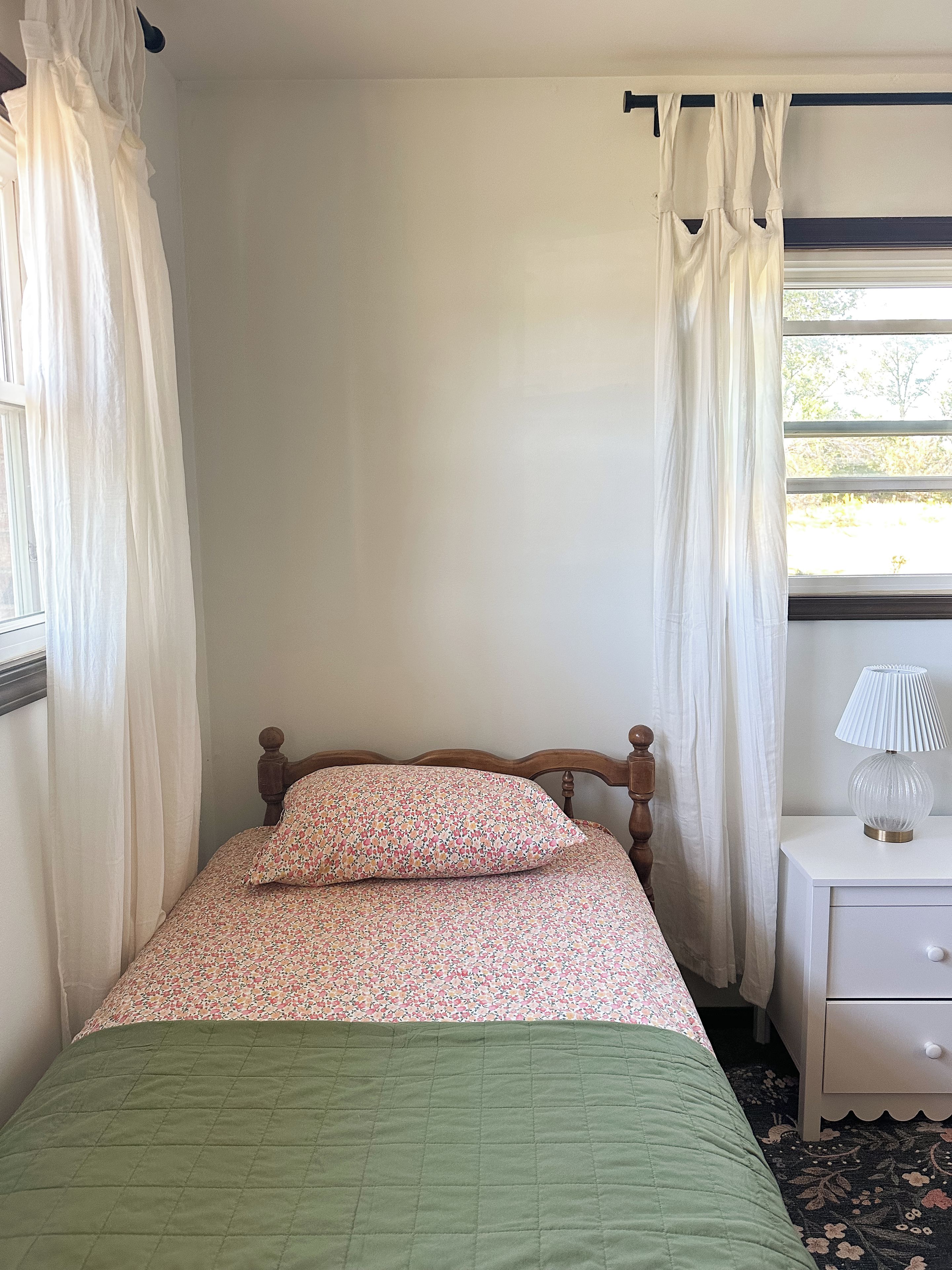 A bedroom with a bed, a nightstand, a lamp, and sheer curtains.
