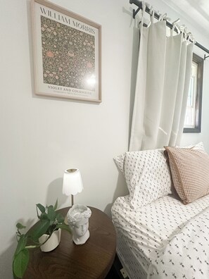 A room with a framed picture, a lamp, a potted plant, a statue, a bed with patterned bedding, and a window with curtains. - Country getaway + private pond (Creal Springs)