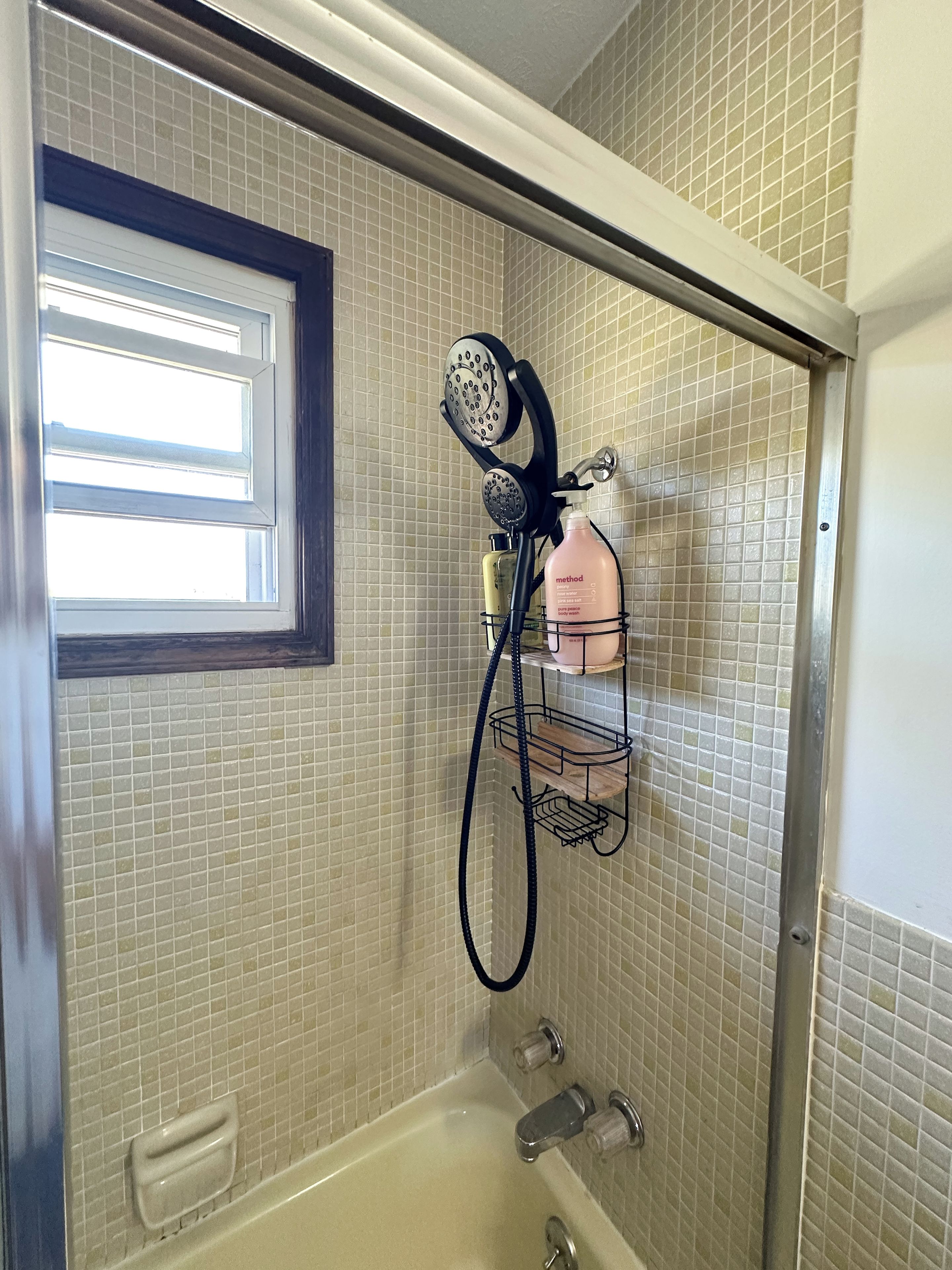 A bathroom with a shower, a window, and a tiled wall.