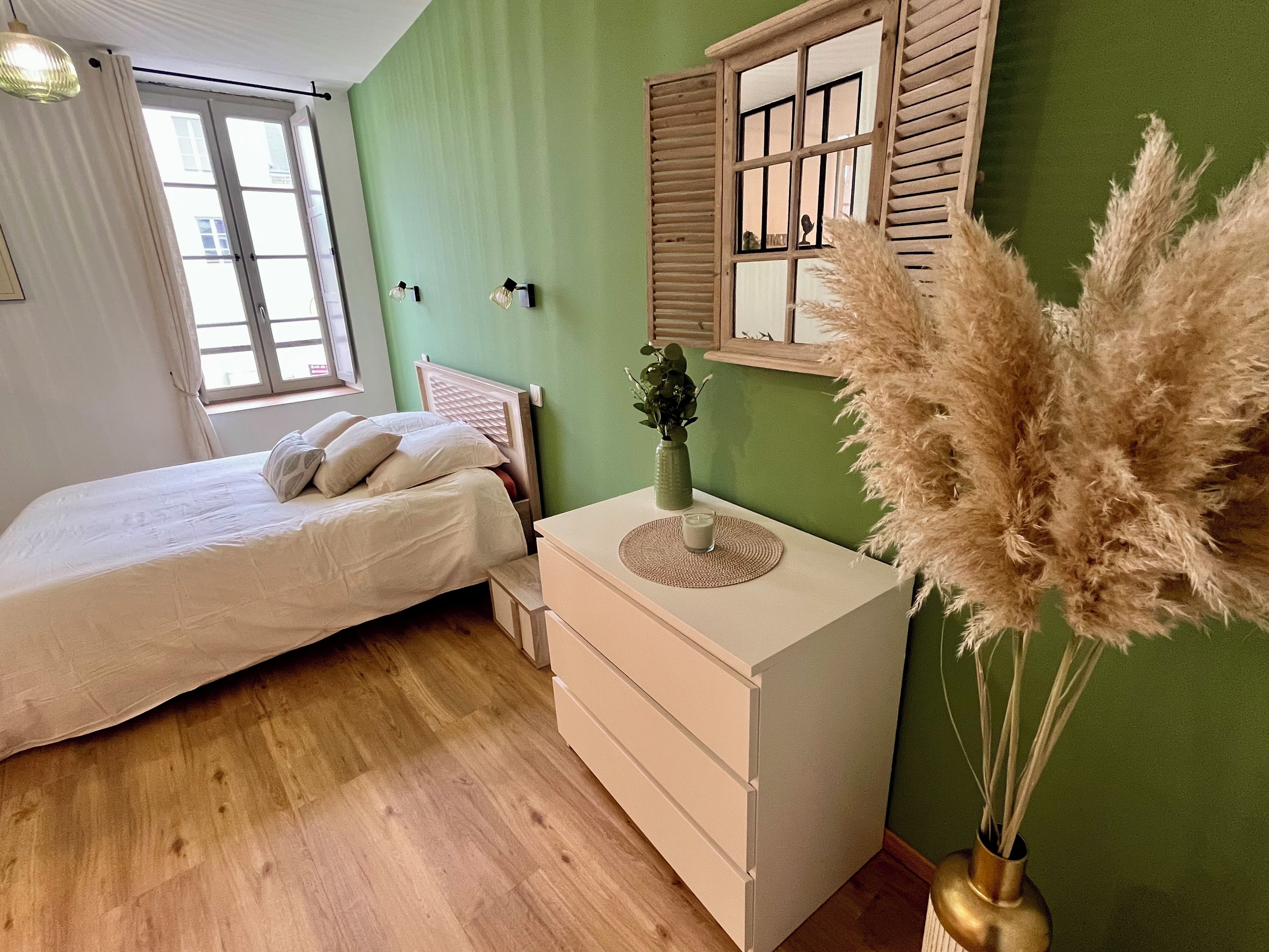 A bedroom with a bed, bedside table, dresser, and a window with curtains.