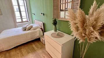 A bedroom with a bed, bedside table, dresser, and a window with curtains.