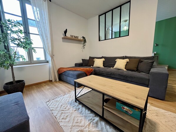 Una sala de estar con sofá, mesa de centro, planta en maceta y ventana con cortinas.