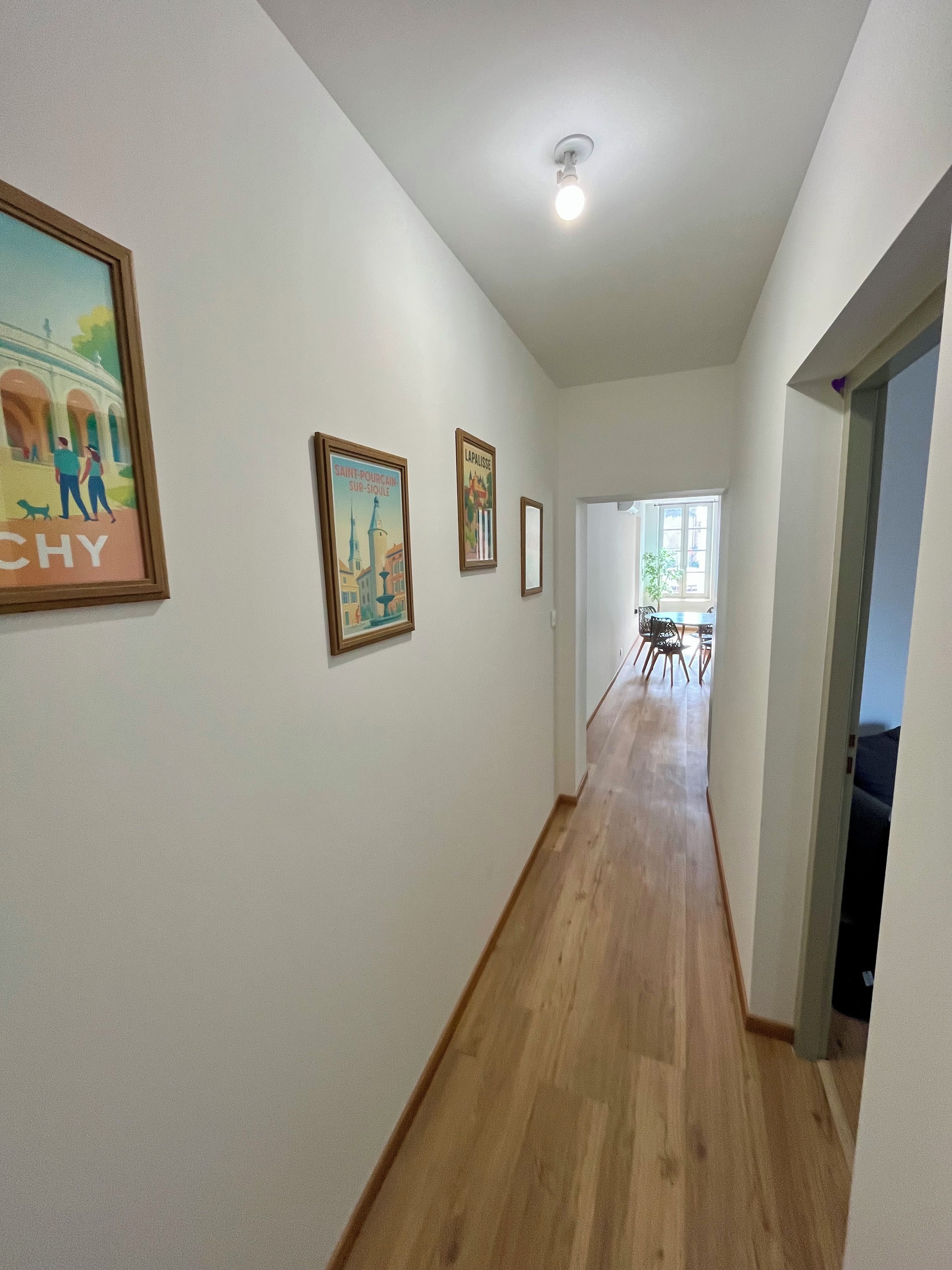 A hallway with wooden flooring, framed pictures on the walls, and a ceiling light.