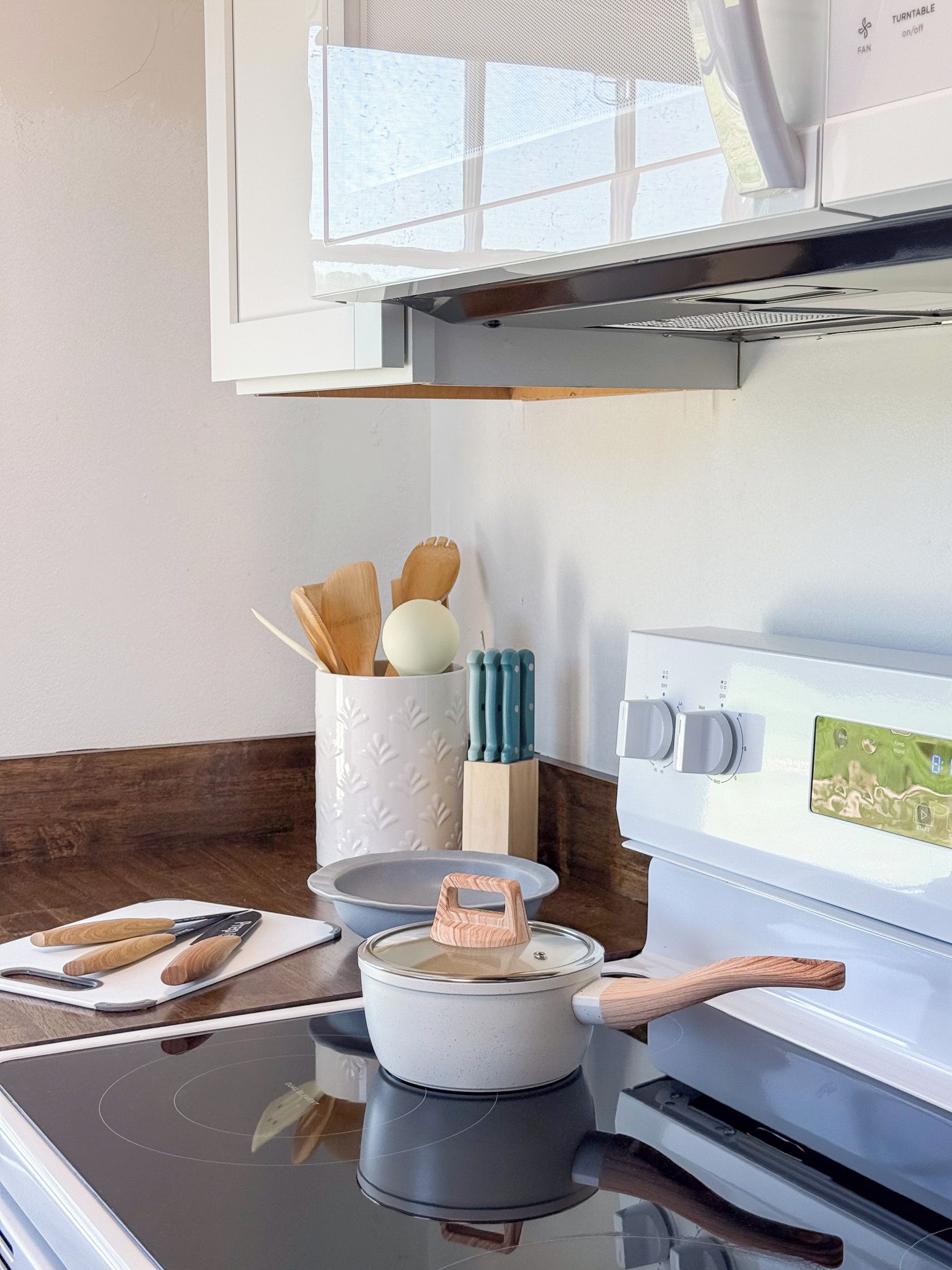 A kitchen with a stove, microwave, and a white cabinet with utensils.