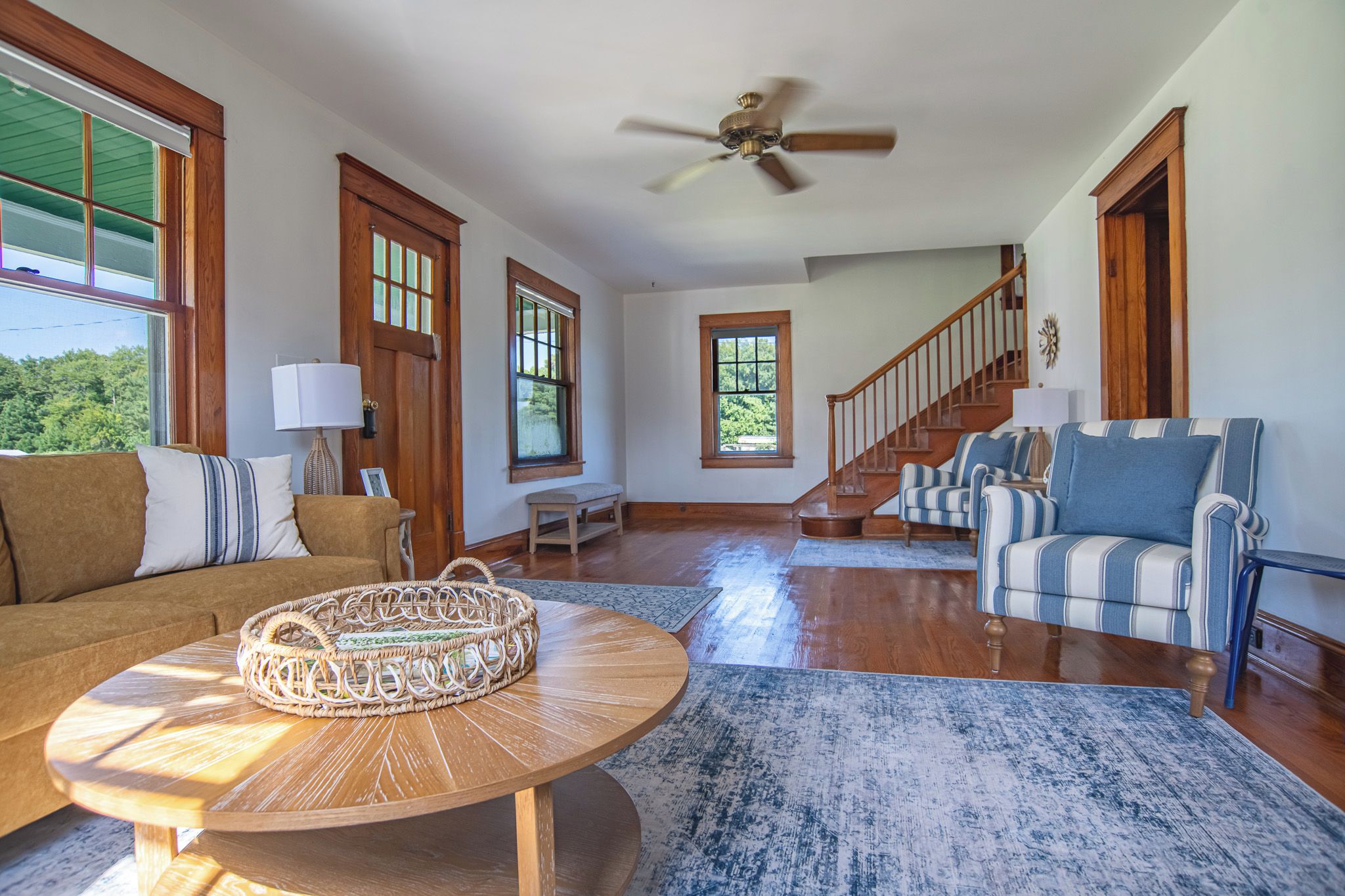 A spacious living room with a wooden floor, a round coffee table, a striped sofa, and a staircase leading to another level.