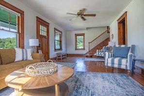 A spacious living room with a wooden floor, a round coffee table, a striped sofa, and a staircase leading to another level. - Marvelous  Farm house style with 3-bedrooms in charming Cape Charles (Cape Charles)