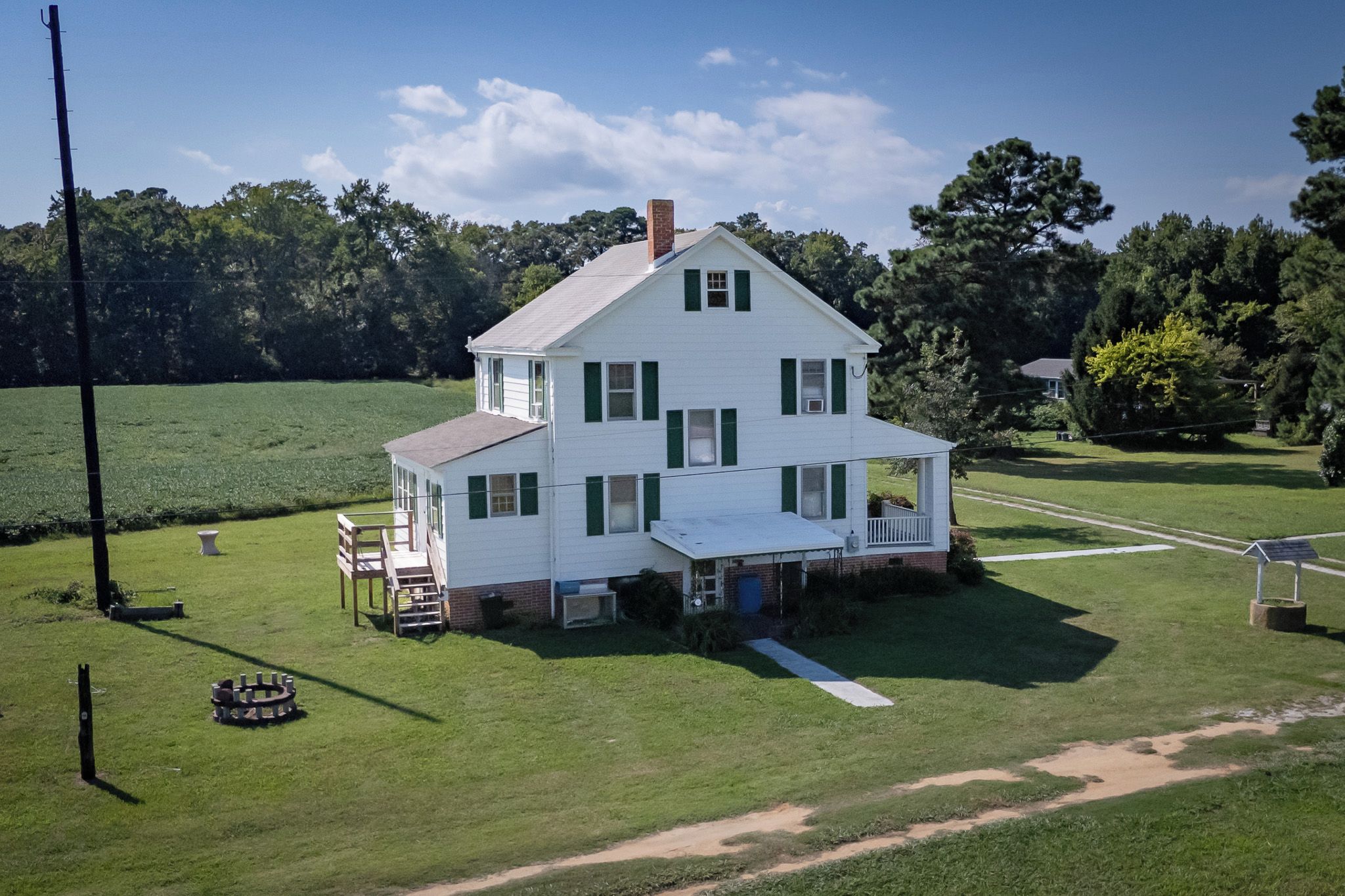A two-story white house with a porch, surrounded by a grassy field and trees.