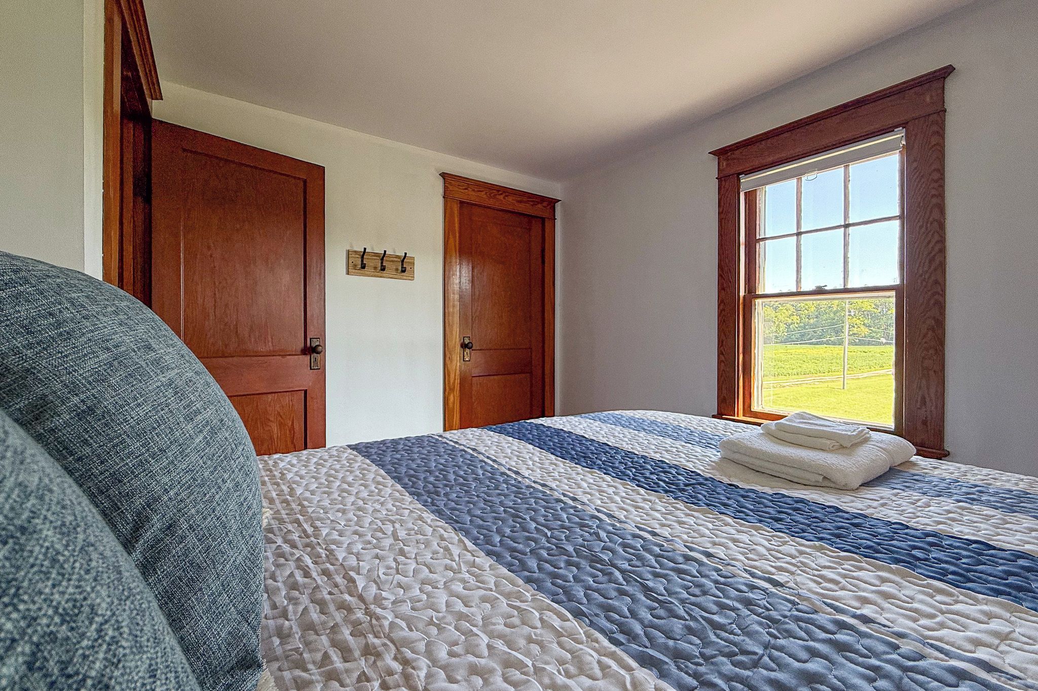 A bedroom with a bed, a window with a view of a field, and two wooden doors.