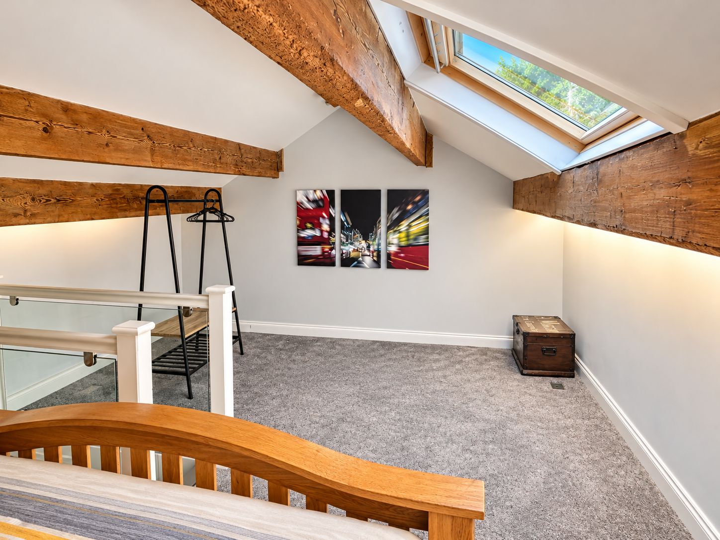 Une pièce avec un plafond en pente, des poutres en bois, un escalier, une petite table et une fenêtre donnant sur les arbres.