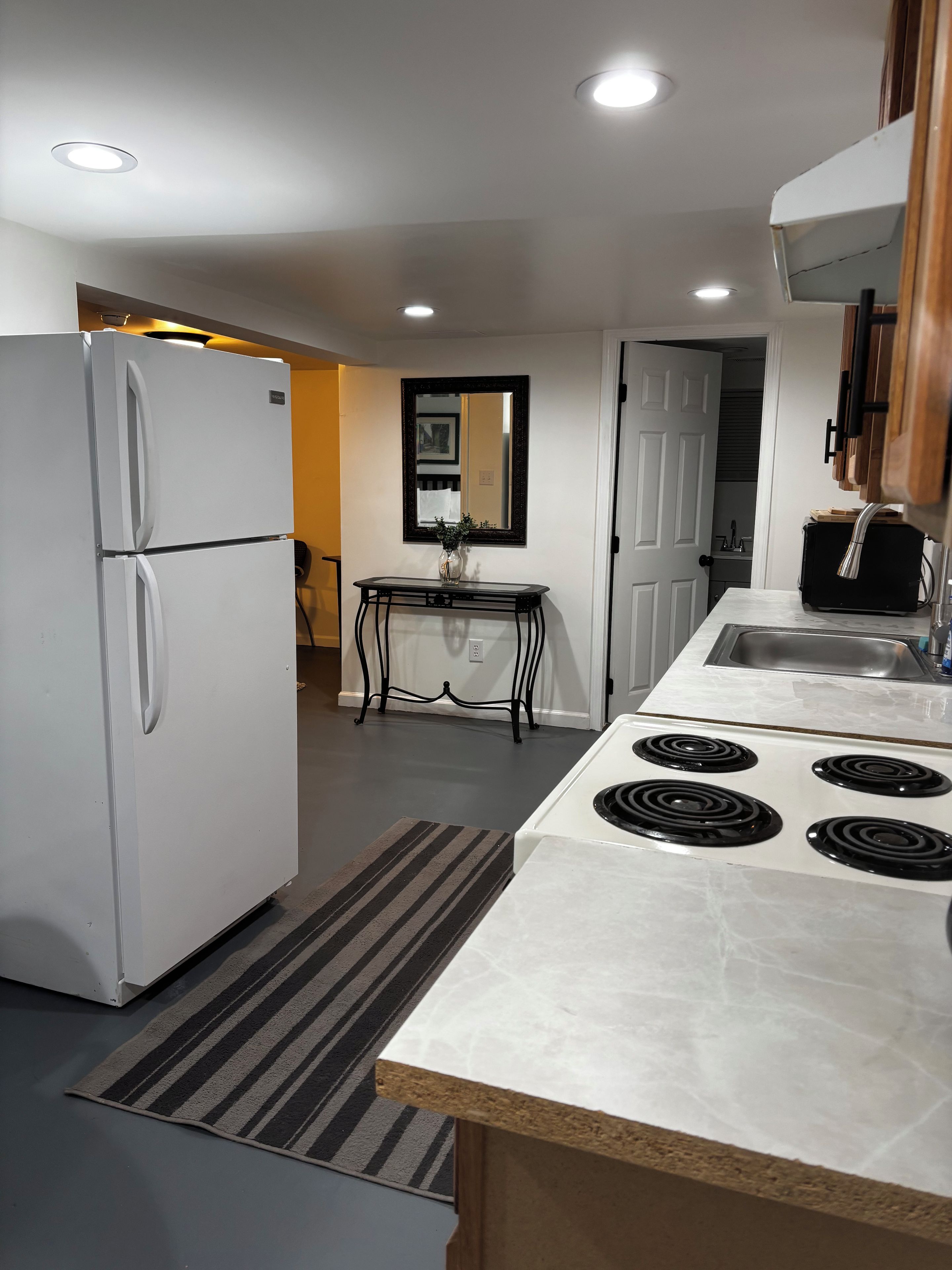Une cuisine compacte avec un réfrigérateur blanc, une cuisinière à quatre brûleurs, une petite table avec un vase et un miroir accroché au mur.