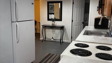 Une cuisine compacte avec un réfrigérateur blanc, une cuisinière à quatre brûleurs, une petite table avec un vase et un miroir accroché au mur.