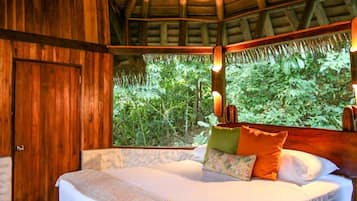 A wooden room with a bed, a door, and a view of greenery outside.