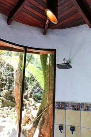 Una habitación con techo de madera, pared de azulejos y ventana con vista a un árbol y rocas.