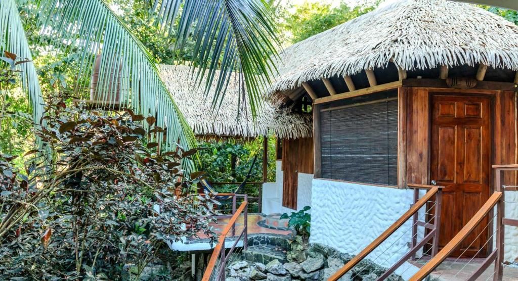 A tropical-style building with a thatched roof, a wooden door, and a stone pathway leading to a wooden staircase.