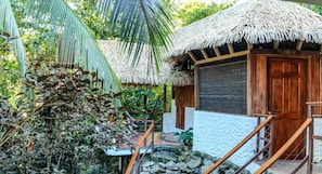 Un edificio de estilo tropical con techo de paja, puerta de madera y un camino de piedra que lleva a una escalera de madera.