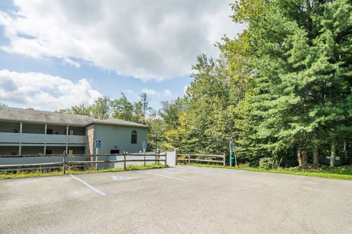 A building with a parking lot, a wheelchair-accessible entrance, and a natural surrounding.