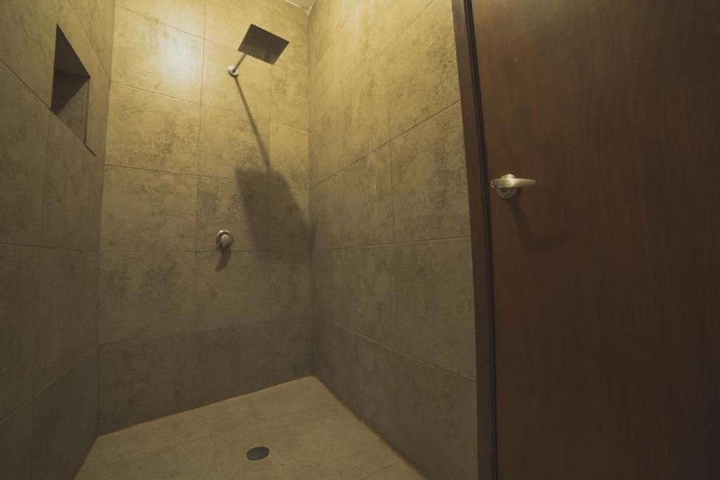 A shower with a handheld showerhead, a drain, and a door with a handle.