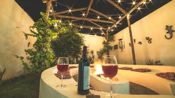 A cozy outdoor seating area with a fire, two wine glasses, and a bottle of wine.