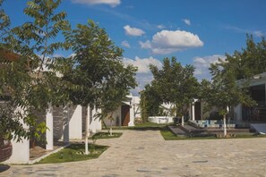 Un patio con un sendero empedrado, edificios blancos y árboles verdes.