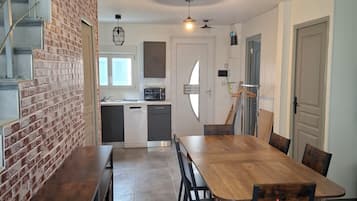 A modern kitchen with a brick accent wall, a dining area with a wooden table and chairs, and a staircase leading to an upper level.