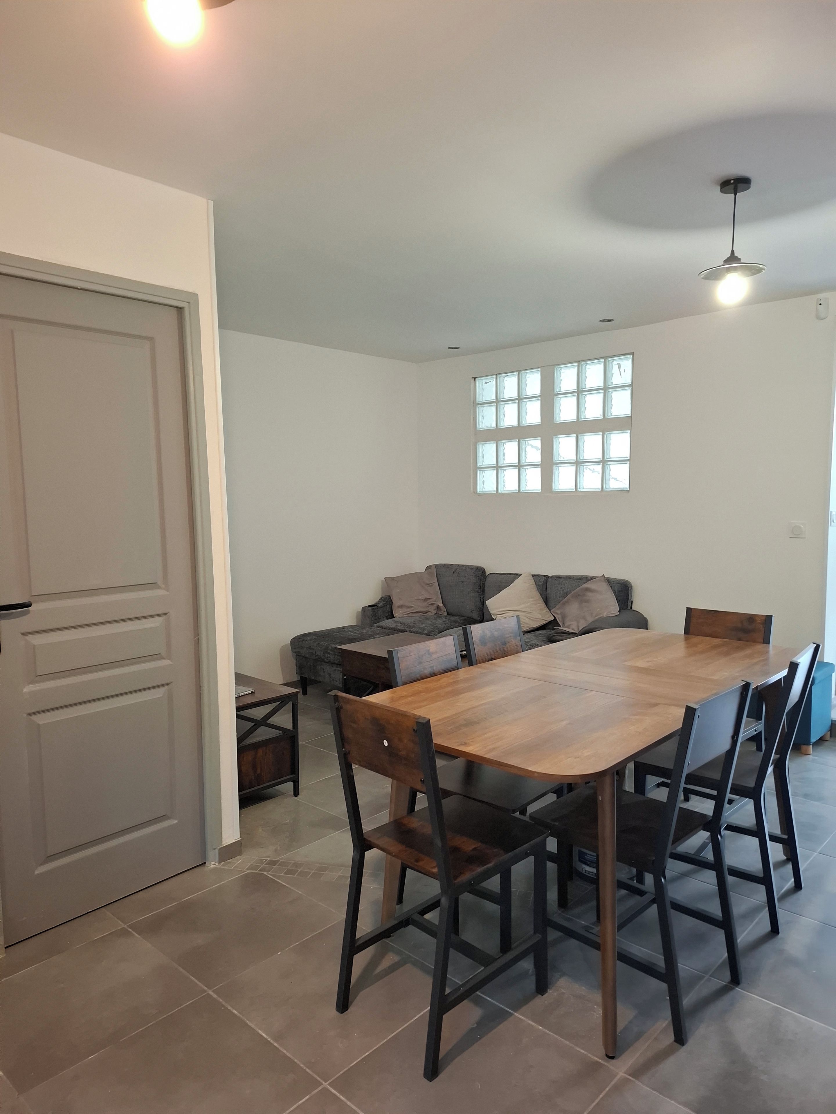 A dining area with a wooden table and chairs, a sofa, and a window with multiple panes.