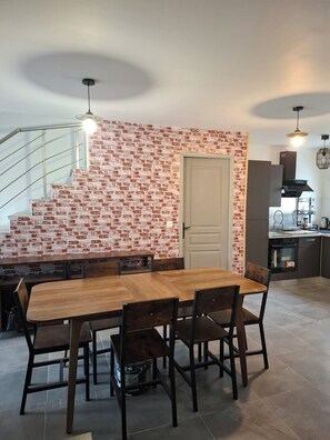 A dining area with a brick wall, a staircase, and a kitchen in the background. - New Listing (Le Val-Saint-Germain)