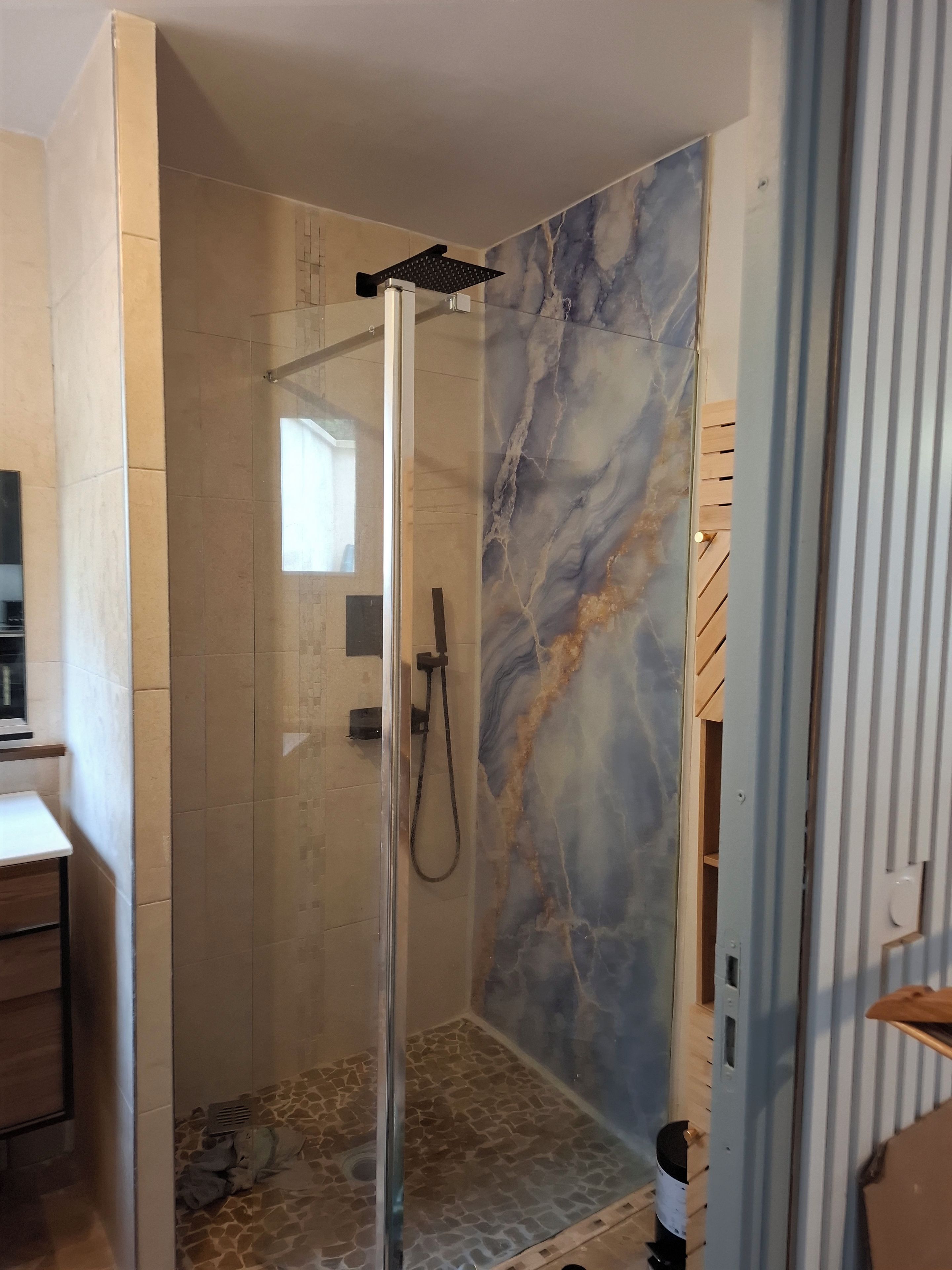 Eine Dusche mit Glastür, Marmorwand und Holzboden.